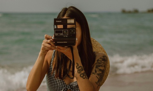 a woman sitting on a beach taking a picture near the ocean