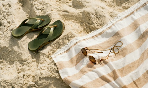 pair of sandals, a towel, and sunglasses on the beach